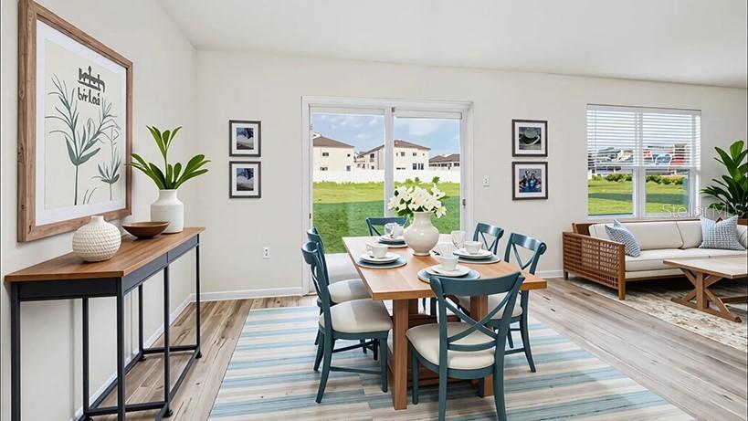 This open-concept dining and living area features light wood flooring, a wooden table, and sliding doors — 10182 SE 158TH LANE, SUMMERFIELD, FL