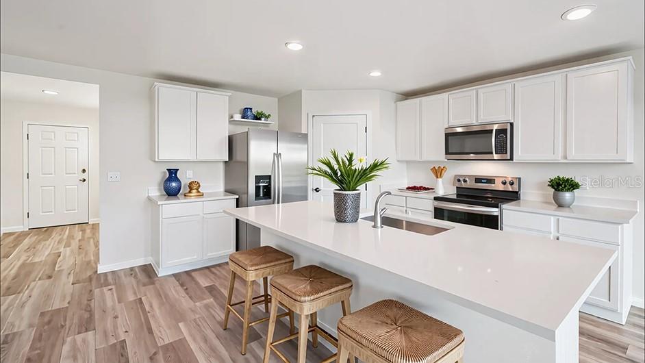 A modern kitchen features white cabinetry, a large island with bar stools, and stainless appliances — 10182 SE 158TH LANE, SUMMERFIELD, FL