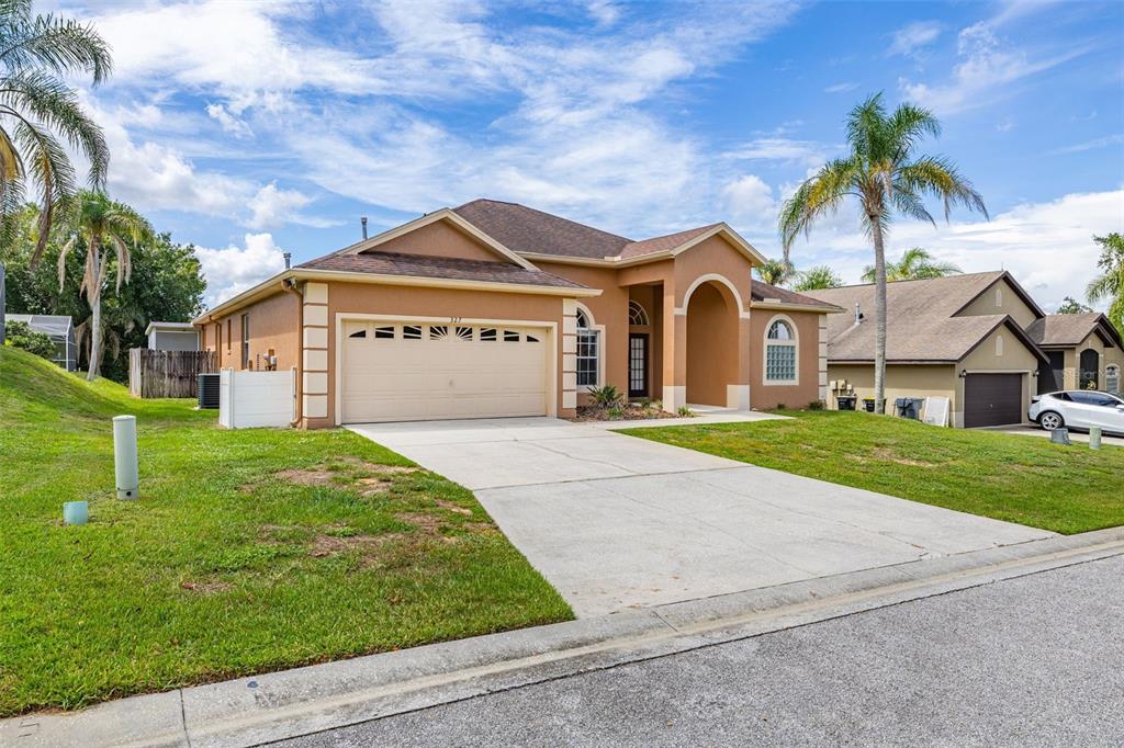 A single-story tan stucco house with a two-car garage and a palm tree in front — 327 GREELEY LOOP, DAVENPORT, FL
