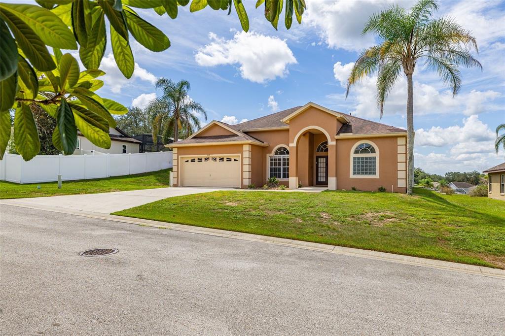 A single-story tan stucco house with a two-car garage and a palm tree in front — 327 GREELEY LOOP, DAVENPORT, FL