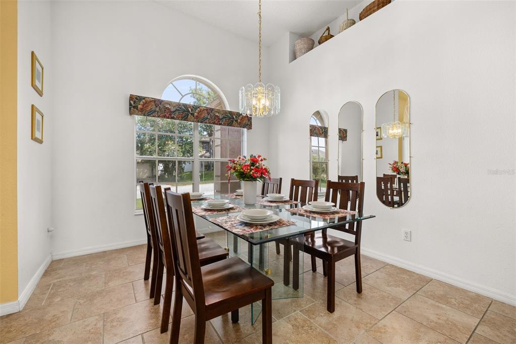 A dining room features a glass-topped table, dark wood chairs, arched mirrors, and tile flooring — 327 GREELEY LOOP, DAVENPORT, FL