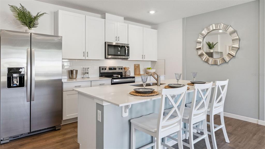 A modern kitchen features white cabinetry, stainless steel appliances, and a central island with seating — 2516 KINSALE LANE, ORMOND BEACH, FL
