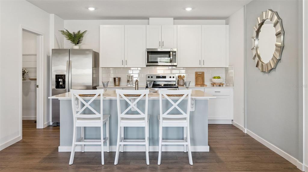 A kitchen features white cabinets, stainless steel appliances, a light blue island, and three chairs — 2516 KINSALE LANE, ORMOND BEACH, FL