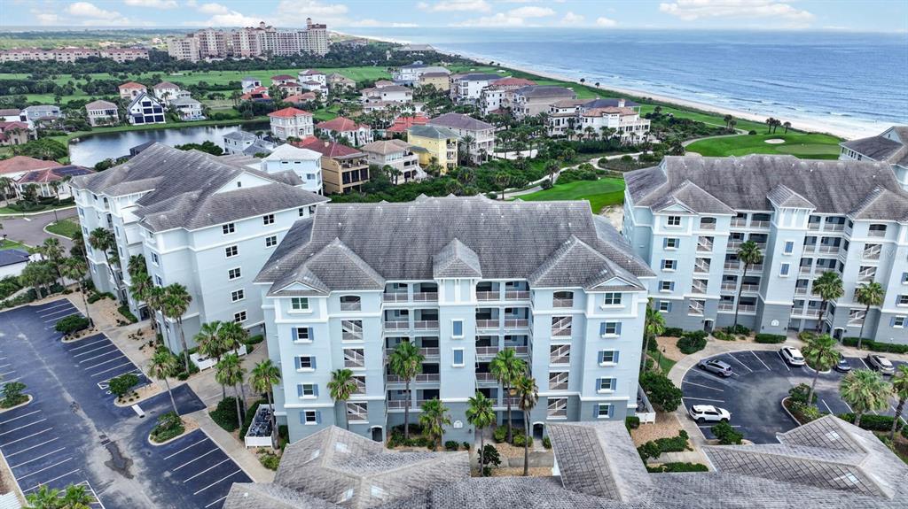 An aerial view shows beachfront condominiums, a golf course green, and surrounding residential homes — 300 CINNAMON BEACH WAY UNIT 221, PALM COAST, FL