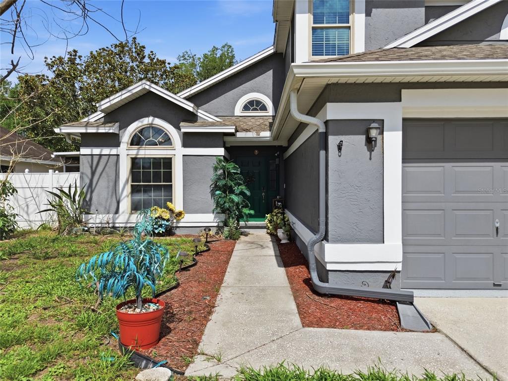 A gray house exterior features a front walkway, a green door, and a garage — 1621 SPINNING WHEEL DRIVE, LUTZ, FL