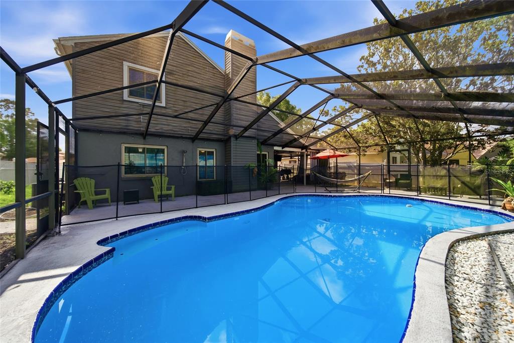 A swimming pool with a safety fence is enclosed by a screened-in lanai — 1621 SPINNING WHEEL DRIVE, LUTZ, FL