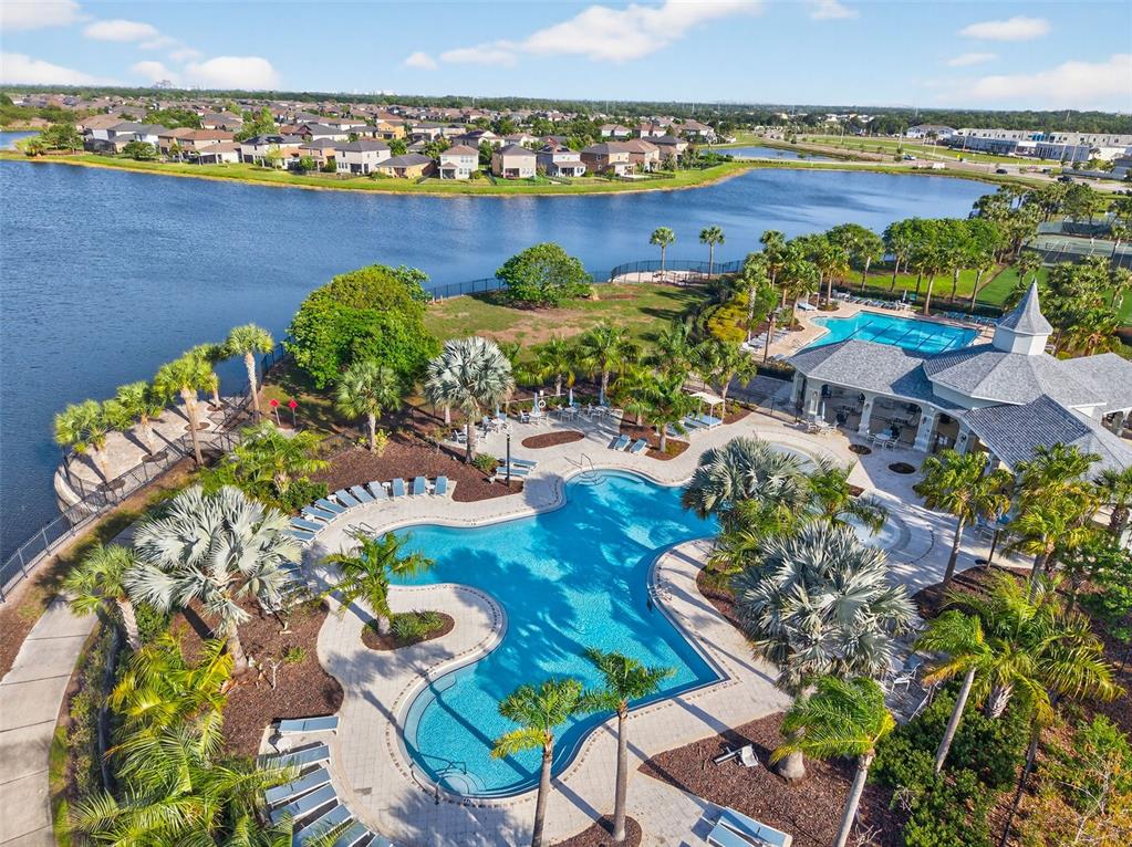 An aerial view shows a community swimming pool and clubhouse located beside a large lake — 9324 LEMON DROP LOOP, SUN CITY CENTER, FL
