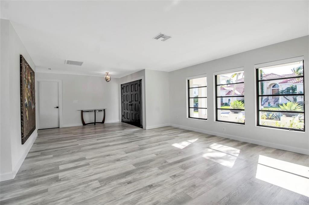 A bright room with light wood-look flooring, three large windows, and a dark paneled door — 1649 STANFORD LANE, SARASOTA, FL