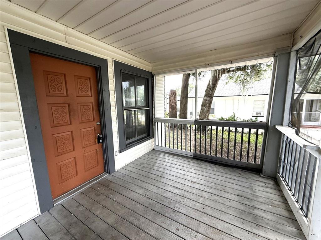 A covered wooden porch features a brown door with decorative panels and a screened railing — 1010 S DUDLEY AVENUE, BARTOW, FL