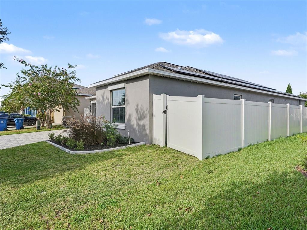 A gray house exterior features a white vinyl privacy fence and a small landscaped garden — 149 TAFT DRIVE, DAVENPORT, FL