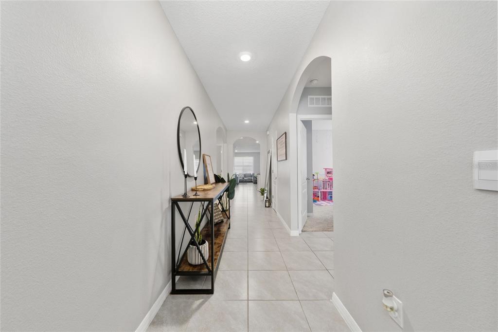A long hallway with light tile flooring, gray walls, and a console table with a mirror — 2845 ETHAN HAMMOCK ROAD, HARMONY, FL