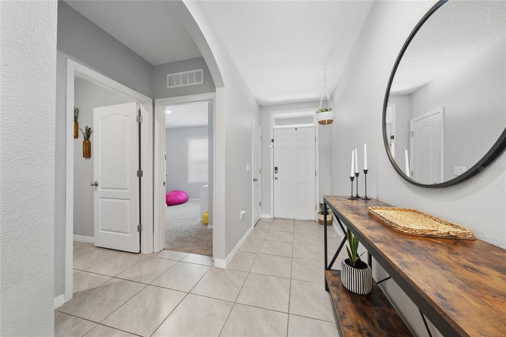 A tiled entryway features a console table, a round mirror, and doorways leading to rooms — 2845 ETHAN HAMMOCK ROAD, HARMONY, FL