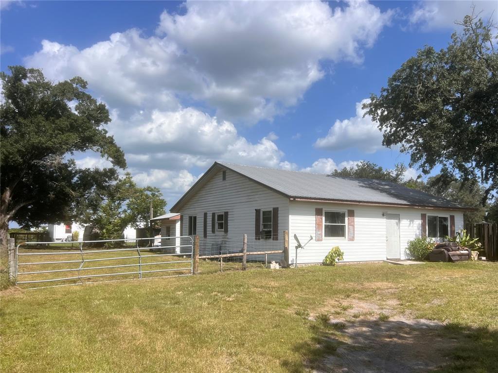 A single-story white house with a metal roof sits on a grassy lot with fencing — 6586 NE MOORE AVENUE, ARCADIA, FL