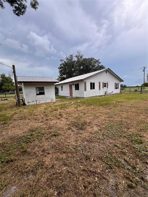 A white house with a metal-roofed shed stands on a grassy lot under a cloudy sky — 6586 NE MOORE AVENUE, ARCADIA, FL