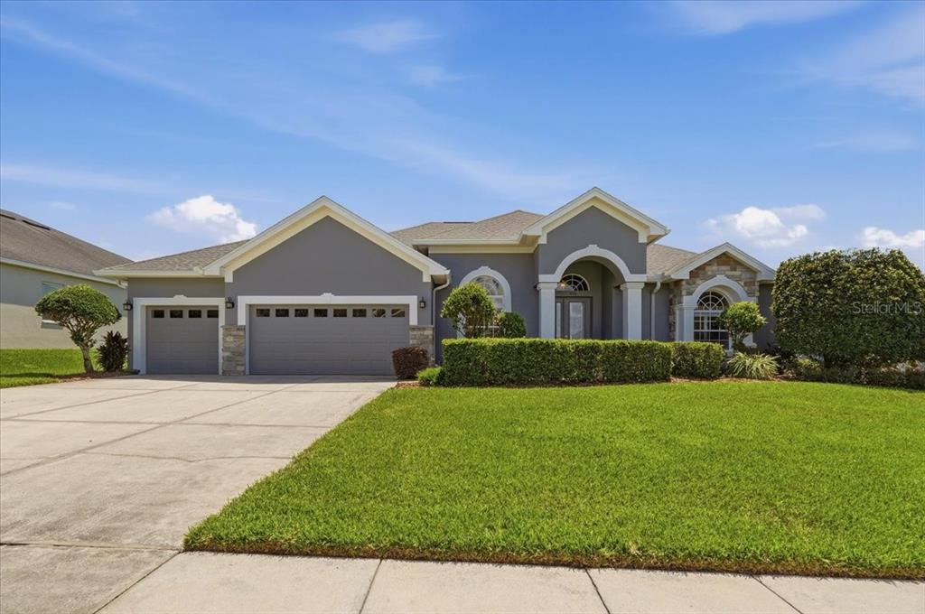 A gray single-story house with a three-car garage and a manicured front lawn — 230 LAKE ARIETTA COURT, AUBURNDALE, FL