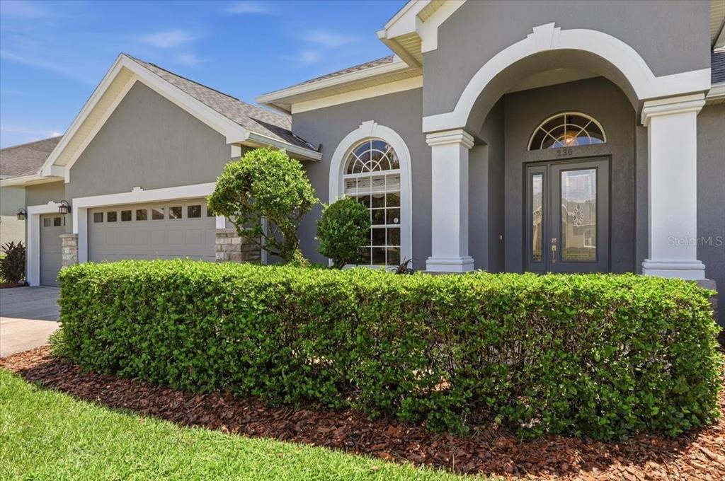 A gray house exterior features a front door with a transom window and a hedge — 230 LAKE ARIETTA COURT, AUBURNDALE, FL