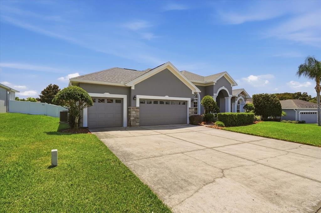 A gray single-story house with a three-car garage and a concrete driveway under a blue sky — 230 LAKE ARIETTA COURT, AUBURNDALE, FL