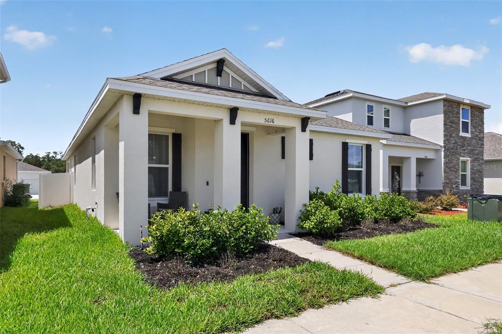A single-story house with a covered front porch, stucco siding, and a small front garden — 5616 BEGGS ROAD, ST CLOUD, FL