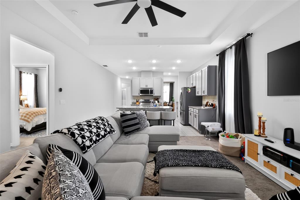 A living room with a gray sectional sofa opens into a kitchen with white cabinetry — 5616 BEGGS ROAD, ST CLOUD, FL
