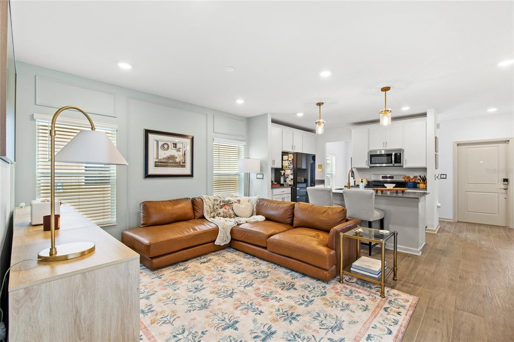 A living room with a brown leather sectional sofa opens into a kitchen with white cabinets — 6002 BLISSFUL STREET, CLERMONT, FL