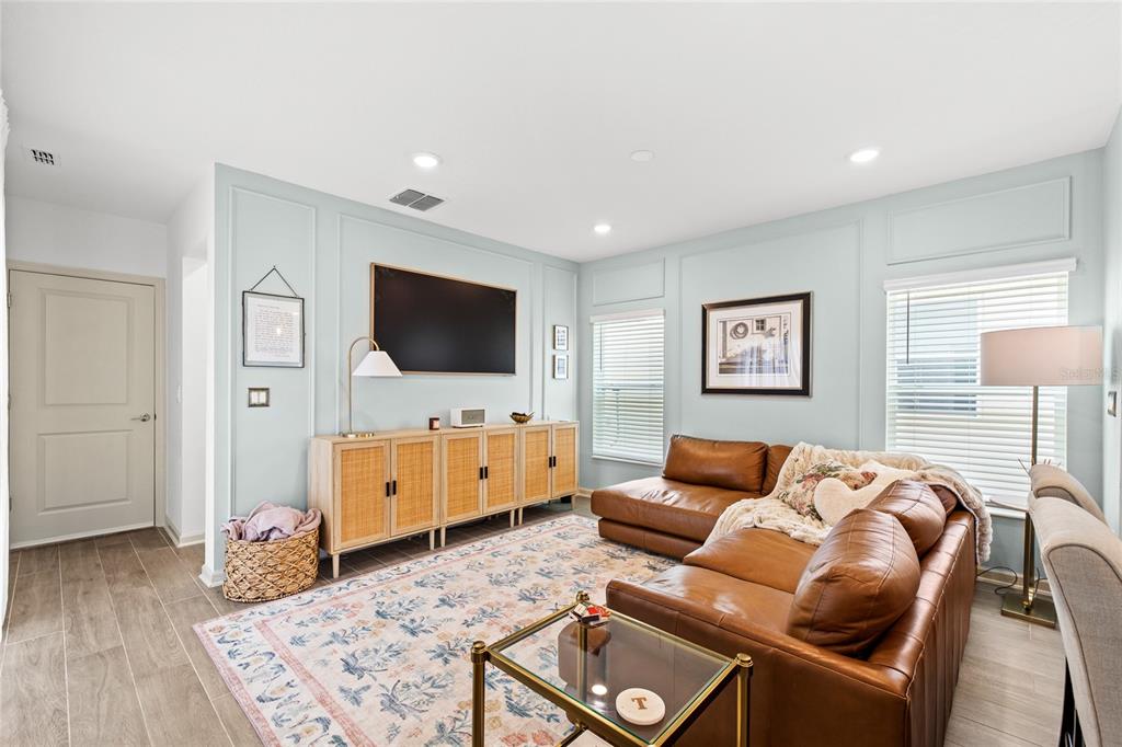 A living room features light blue paneled walls, a brown leather sectional, and a media console — 6002 BLISSFUL STREET, CLERMONT, FL