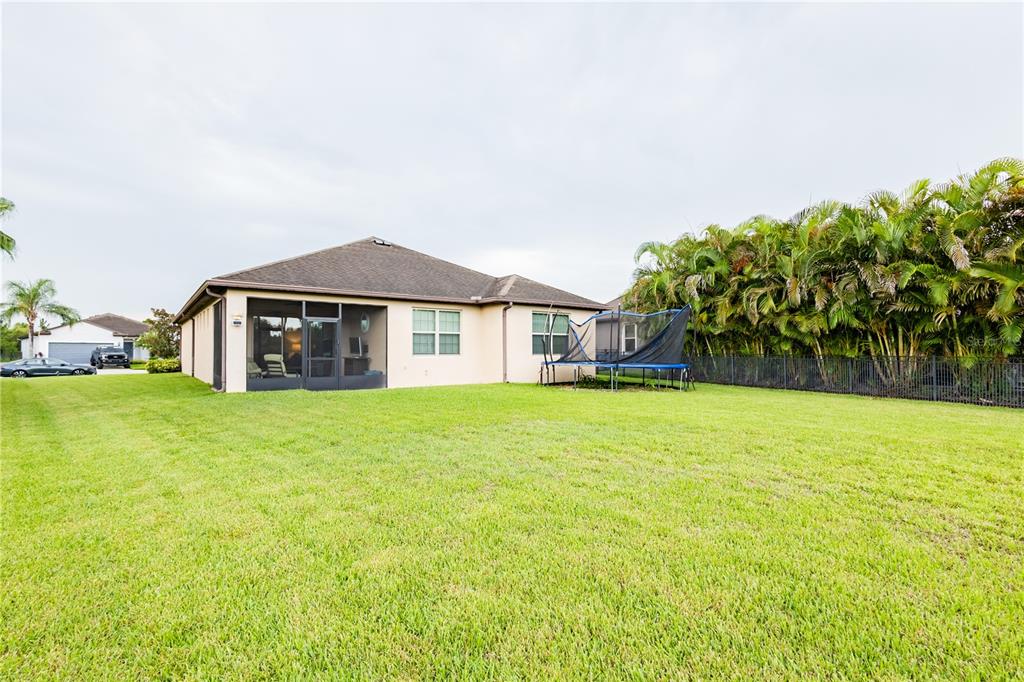 The exterior of a beige house features a screened-in lanai and a large grassy backyard — 10801 52ND COURT E, PARRISH, FL