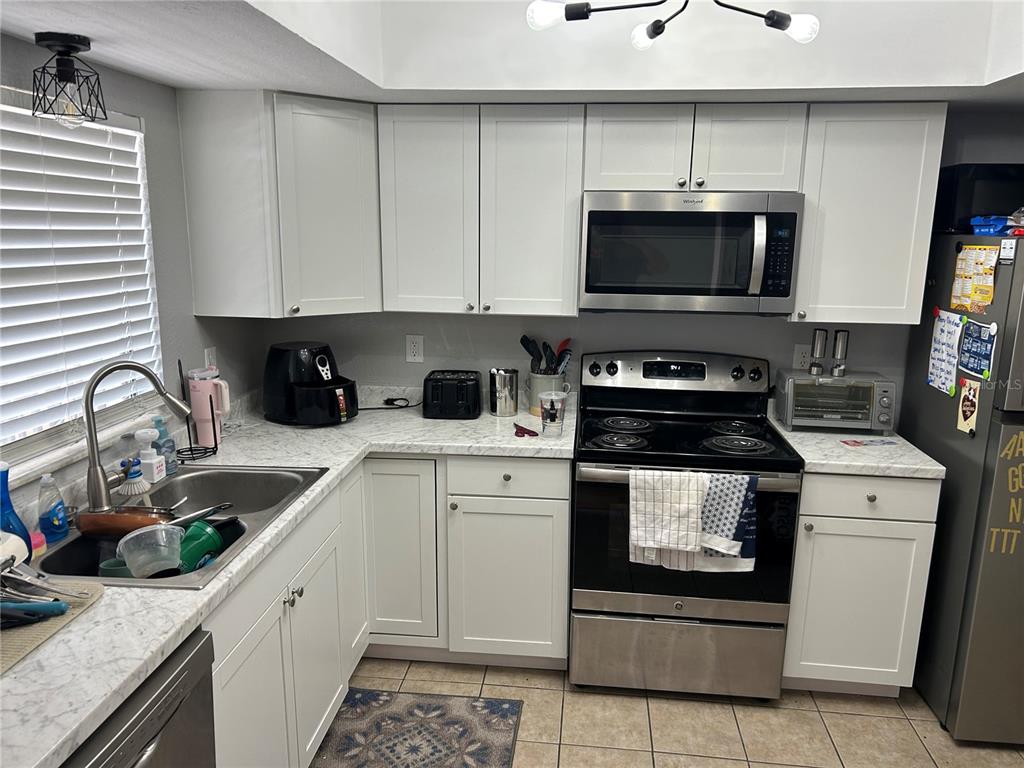 A kitchen features white cabinets, marble-look countertops, stainless steel appliances, and a tile floor — 6301 58TH STREET N UNIT 501, PINELLAS PARK, FL