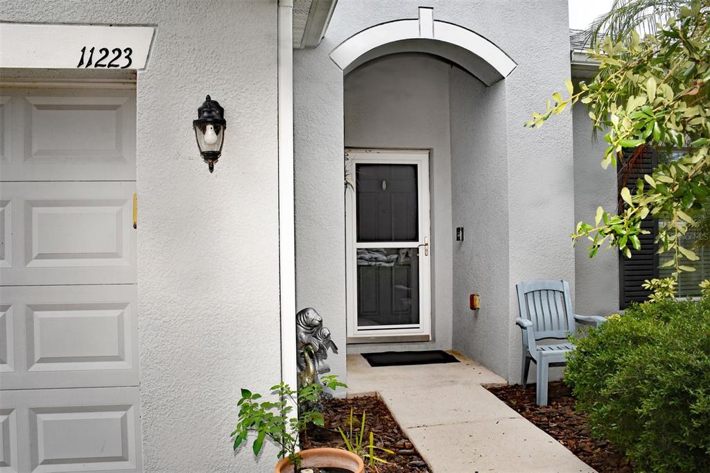 A light-colored house exterior features a front door with a screen, a walkway, and seating — 11223 82ND STREET E, PARRISH, FL