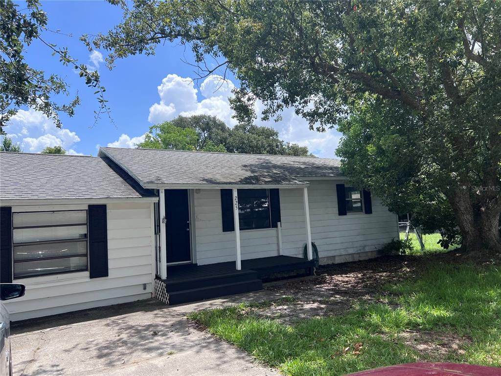 A white single-story house with black shutters and a covered front porch under a tree — 225 MISSISSIPPI AVENUE, ST CLOUD, FL