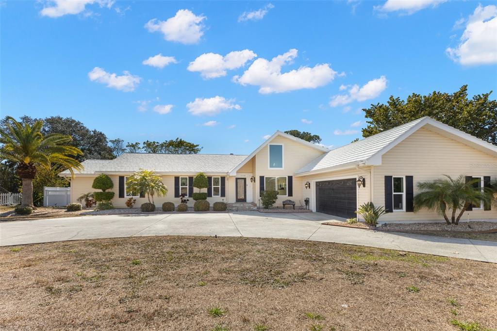 A single-story house with light yellow siding, a dark garage door, and a large driveway — 2138 BAYOU DRIVE, HOLIDAY, FL