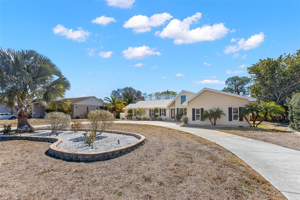 A light yellow house with a concrete driveway and a stone-bordered garden bed — 2138 BAYOU DRIVE, HOLIDAY, FL