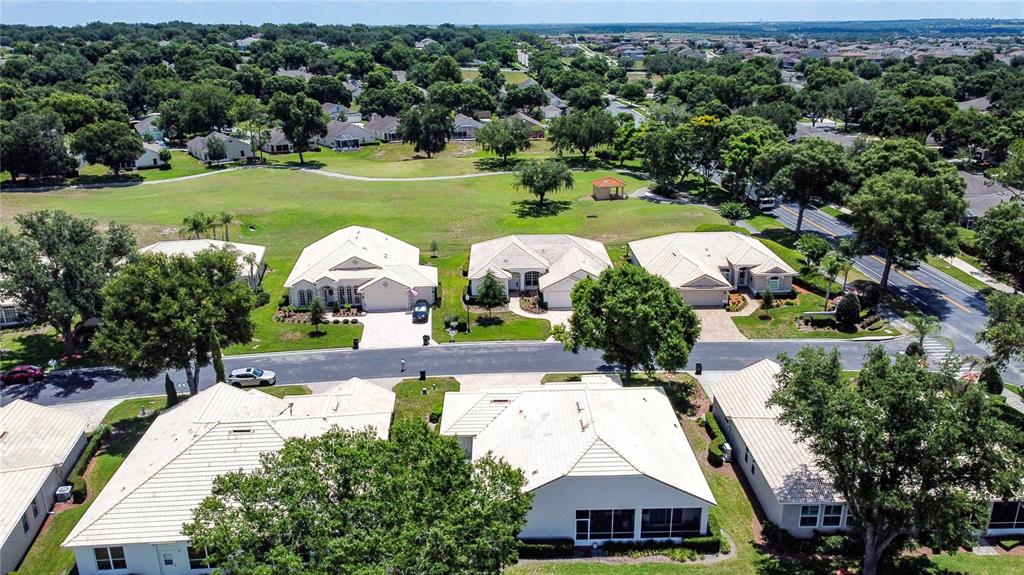 An aerial view shows several suburban houses with light-colored roofs near a grassy park area — 3916 SCARBOROUGH COURT, CLERMONT, FL