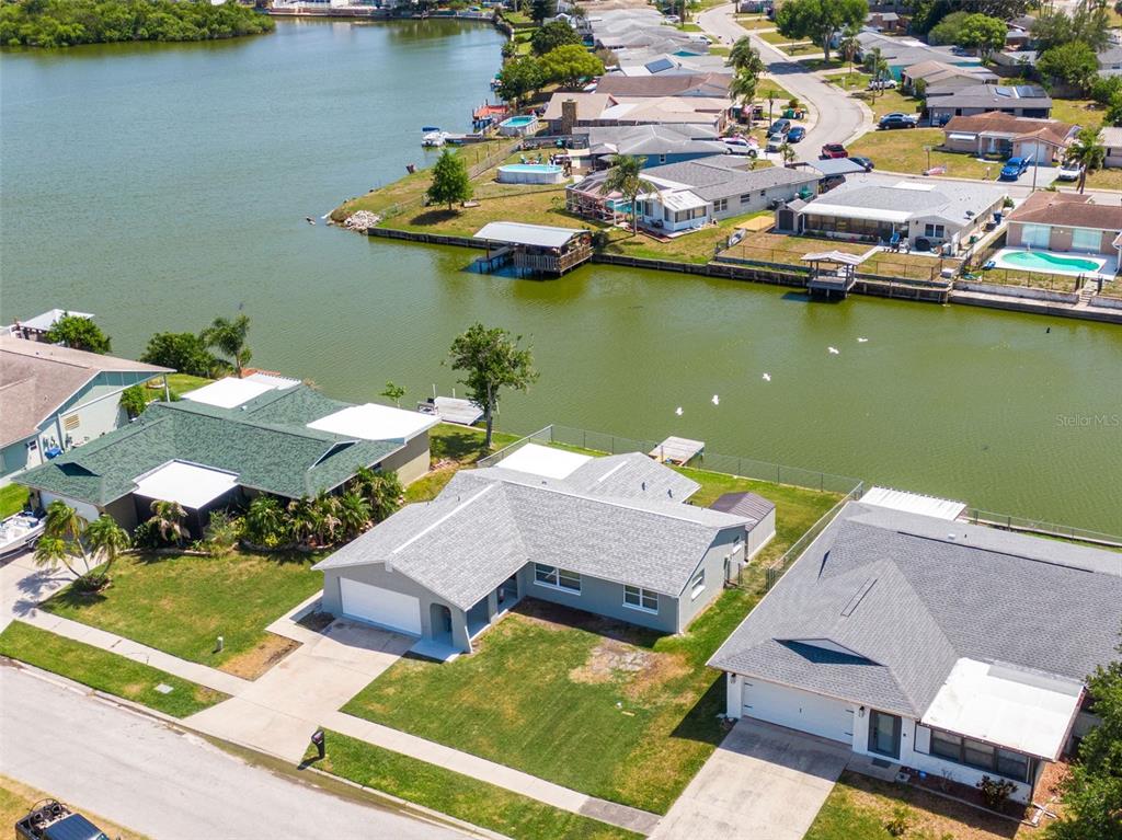 An aerial view shows three suburban houses with gray roofs situated along a waterfront canal — 3132 JACKSON DRIVE, HOLIDAY, FL