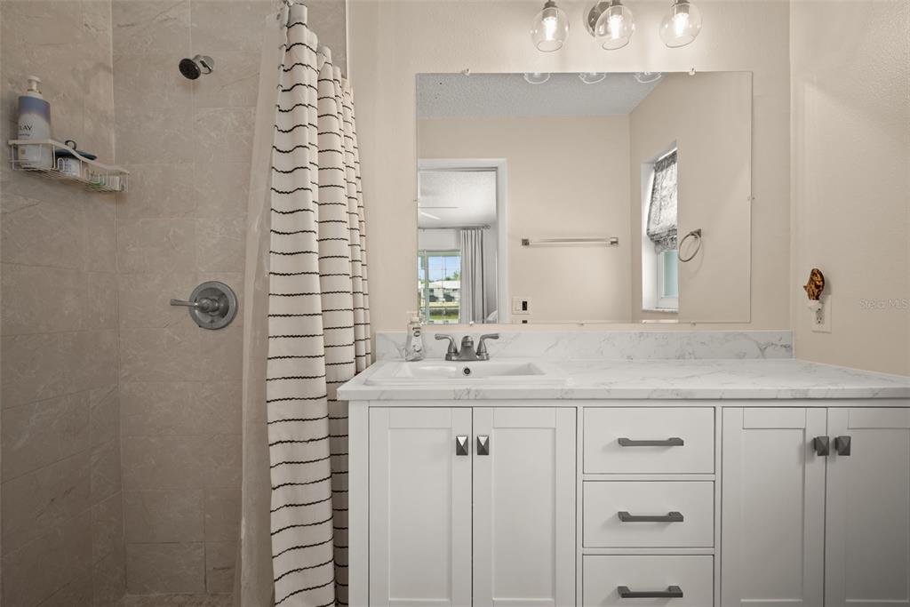 A bathroom features a white vanity with a marble countertop, a mirror, and a tiled shower — 3132 JACKSON DRIVE, HOLIDAY, FL