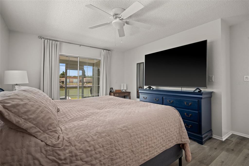 A bedroom features a large bed, a blue dresser with a television, and sliding glass doors — 3132 JACKSON DRIVE, HOLIDAY, FL