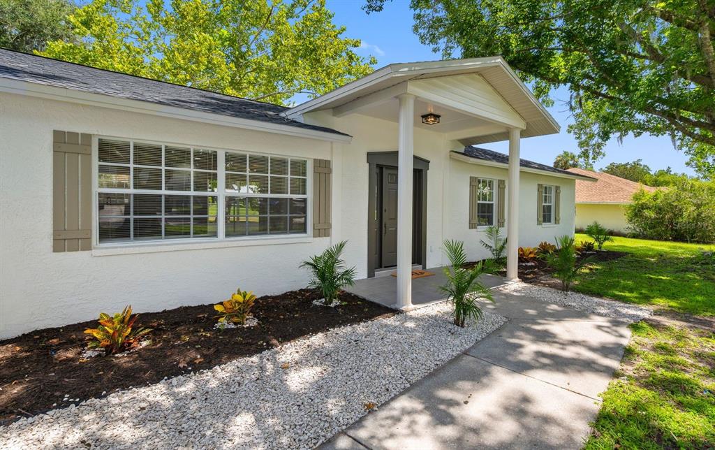 A white house exterior features a covered entryway with columns, shutters, and a landscaped yard — 11836 ORANGE STREET, SAN ANTONIO, FL