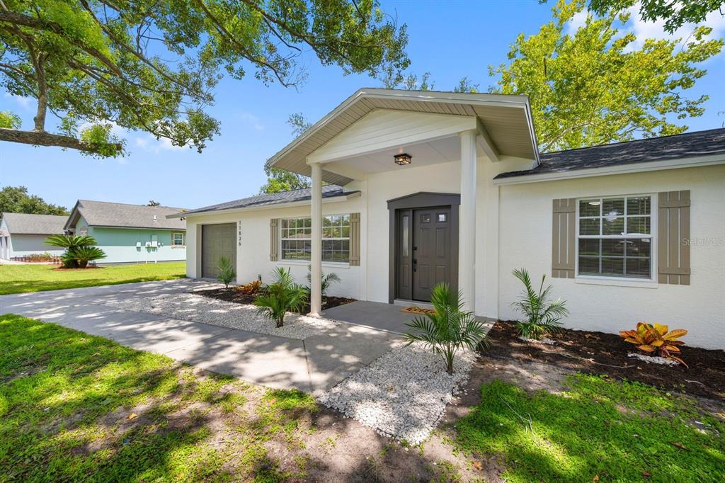 A white single-story house with a covered entryway, dark front door, and gravel landscaping — 11836 ORANGE STREET, SAN ANTONIO, FL