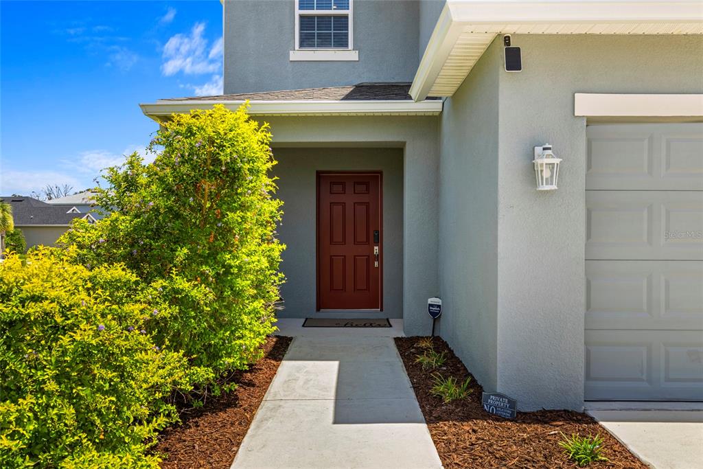A concrete walkway leads to a red front door of a gray house with landscaping — 6365 SPRINGMONT LOOP, PALMETTO, FL