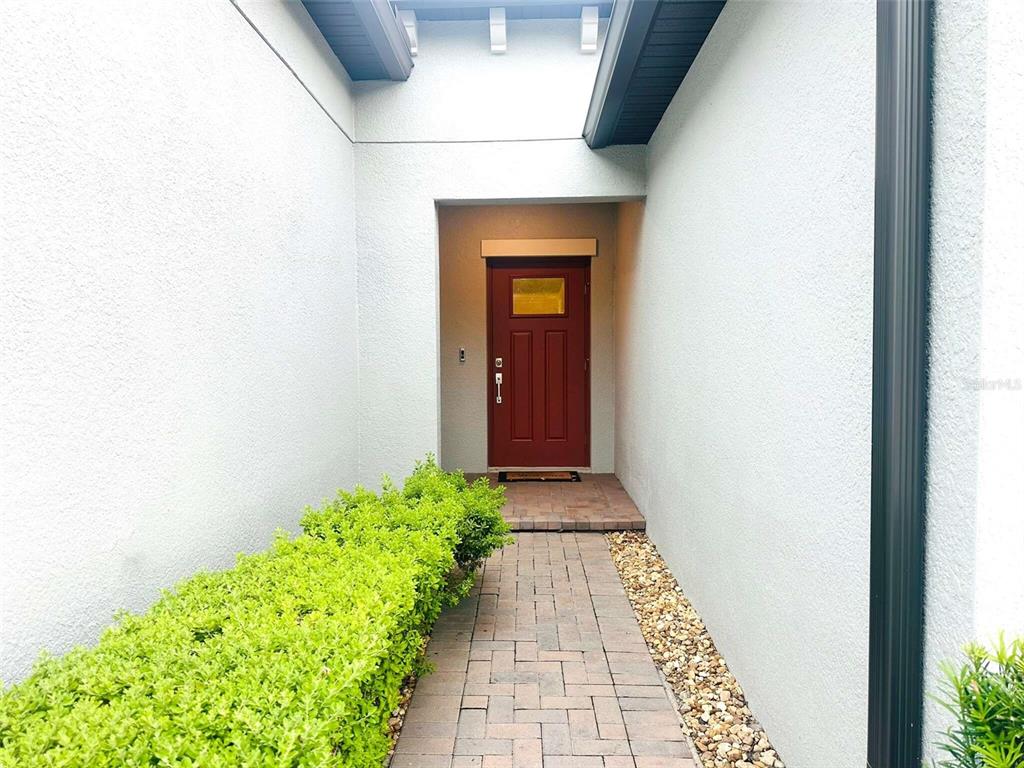 A brick walkway leads to a red front door recessed between two white exterior walls — 16660 SHELL BAY DRIVE, LAND O LAKES, FL