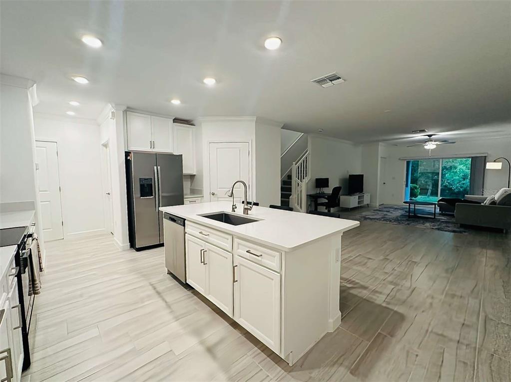 A white kitchen island with a sink sits in an open-concept room with tile flooring — 16660 SHELL BAY DRIVE, LAND O LAKES, FL