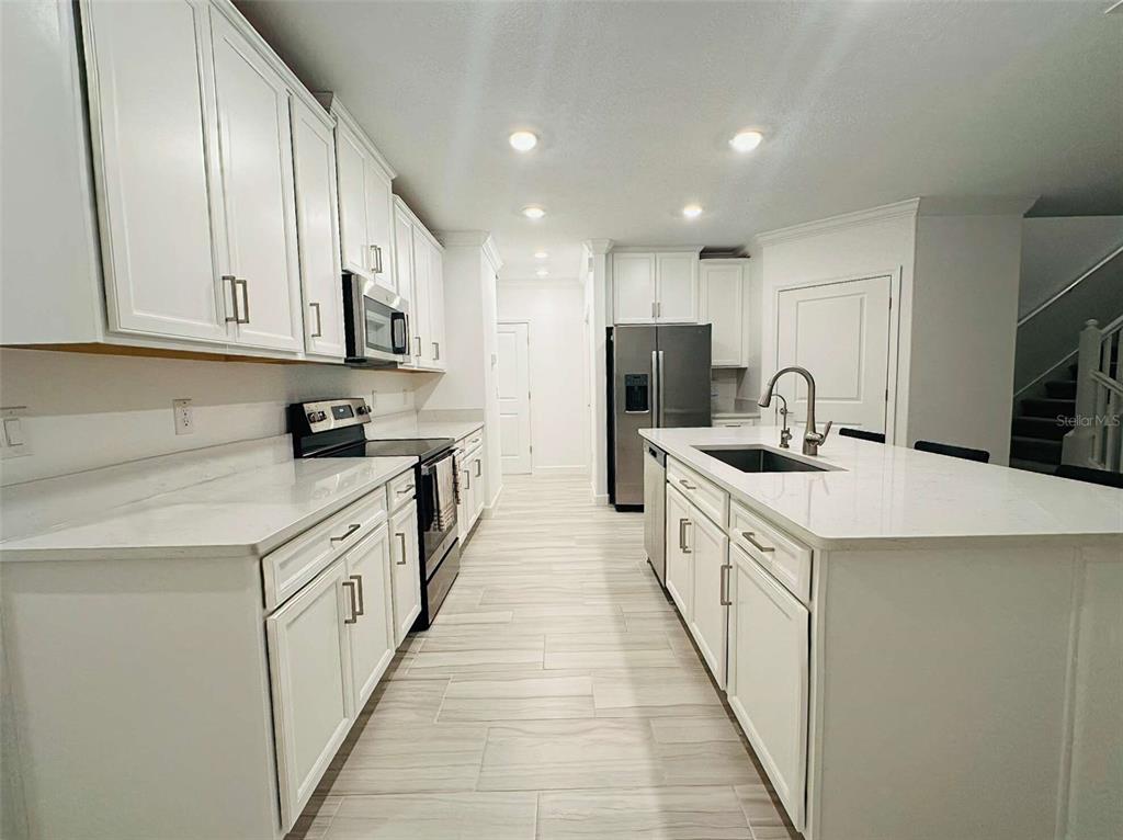 A modern kitchen features white cabinetry, quartz countertops, stainless steel appliances, and light tile flooring — 16660 SHELL BAY DRIVE, LAND O LAKES, FL