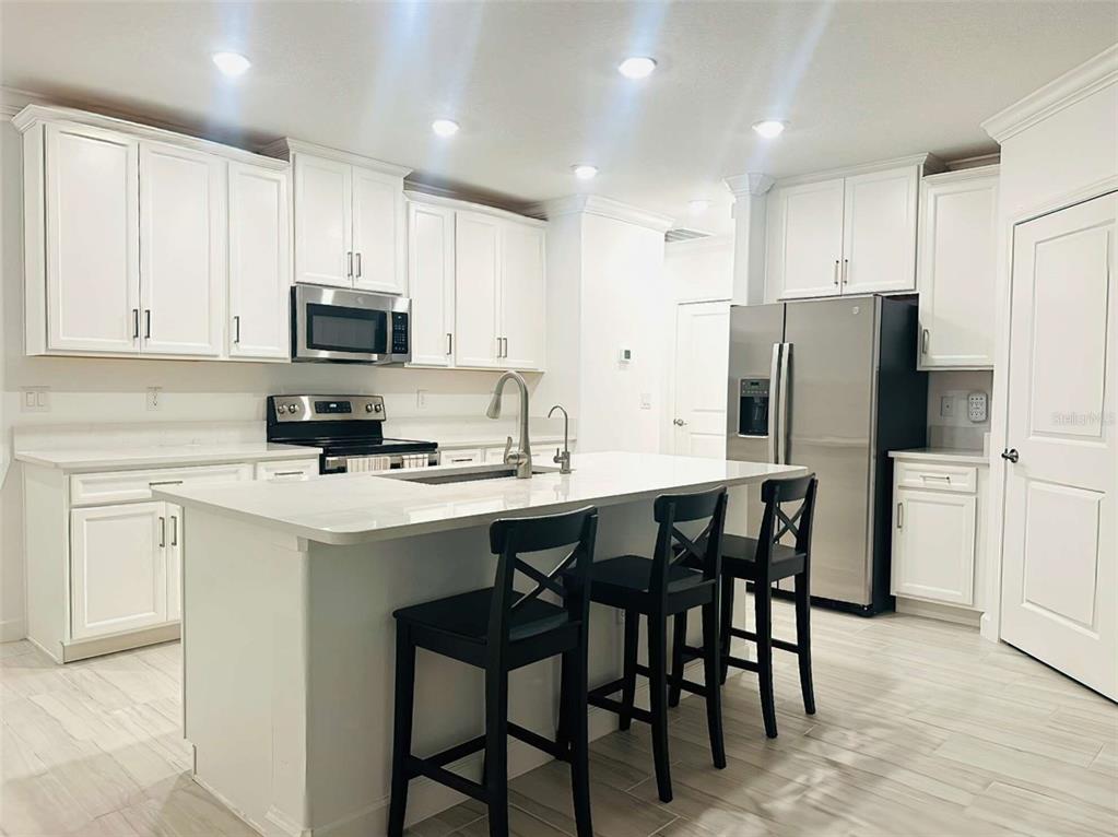 A modern kitchen features white cabinets, stainless steel appliances, a center island, and tile flooring — 16660 SHELL BAY DRIVE, LAND O LAKES, FL