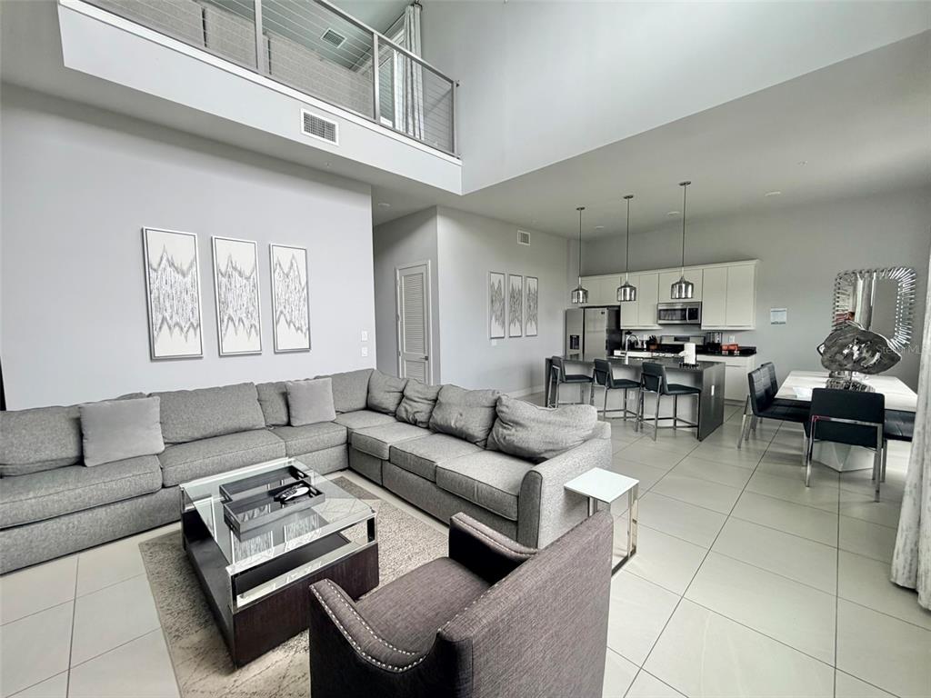 A living room features a large gray sectional sofa, a glass coffee table, and high ceilings — 7770 SANDY RIDGE DRIVE UNIT 207, REUNION, FL