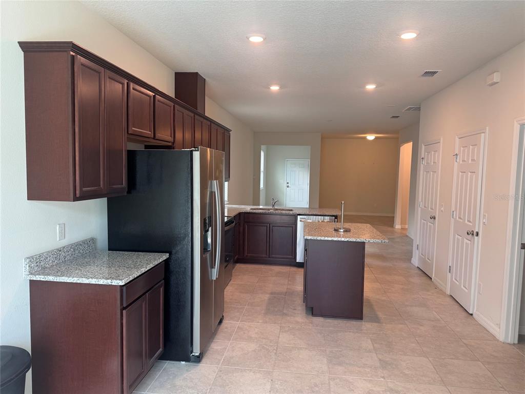 A kitchen features dark wood cabinets, granite countertops, a stainless steel refrigerator, and tile flooring — 5160 CHICKADEE STREET, ST CLOUD, FL