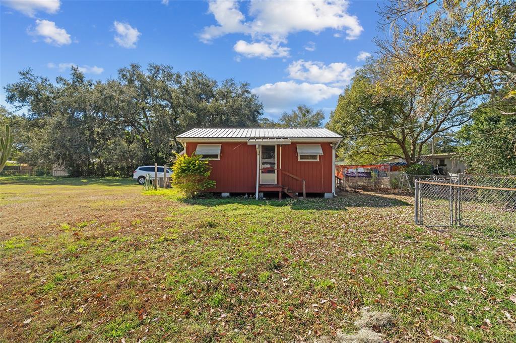 A small red house with a metal roof sits on a grassy lot with trees — 5040 S KALIGA DRIVE, ST CLOUD, FL