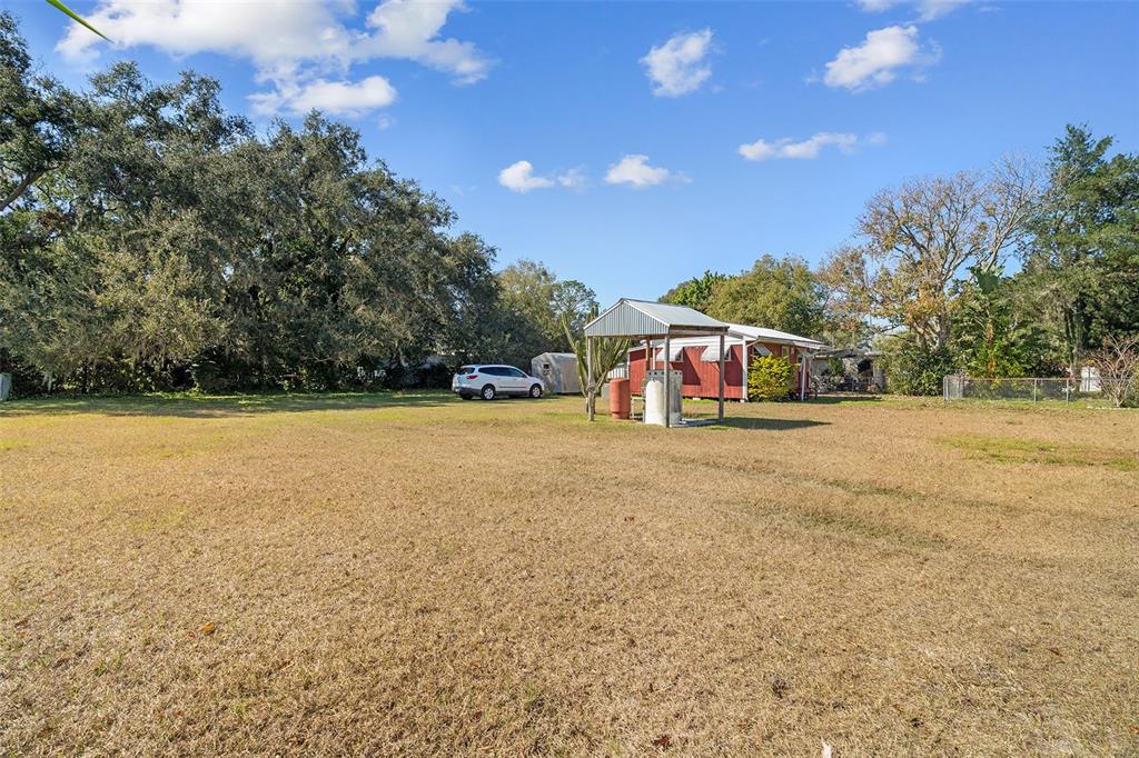 A large, dry grassy yard features a small red building, a carport, and a parked car — 5040 S KALIGA DRIVE, ST CLOUD, FL