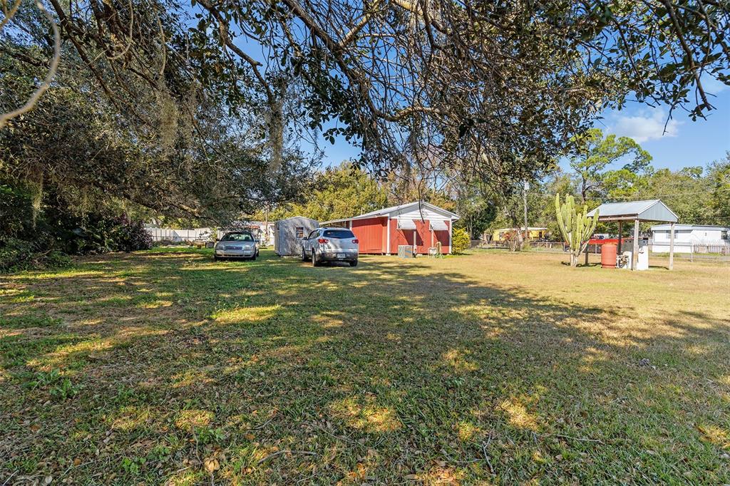 A grassy yard features a red shed, two parked cars, and a small covered structure — 5040 S KALIGA DRIVE, ST CLOUD, FL