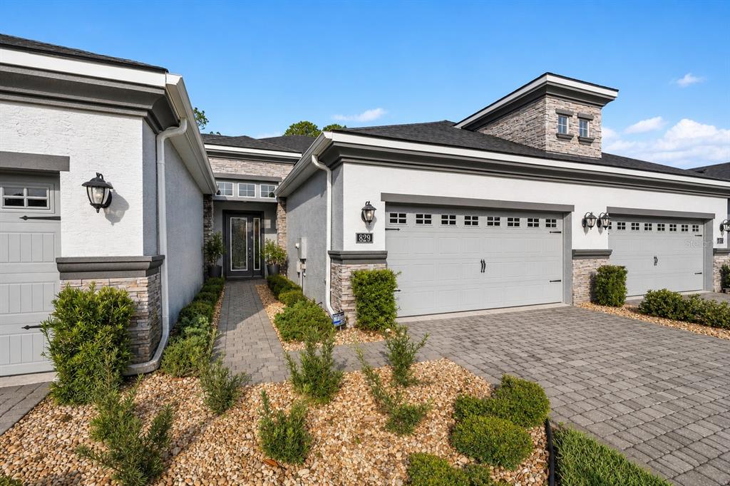 A modern house exterior features a stone-accented facade, a paved driveway, and multiple garage doors — 829 PINEWOOD DRIVE, ORMOND BEACH, FL