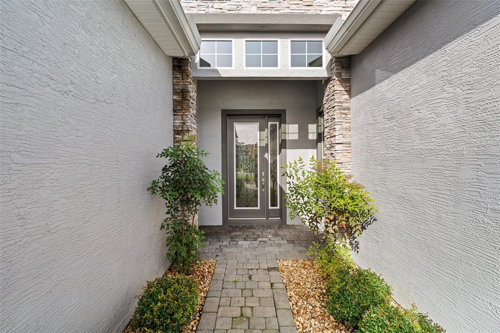 A paved walkway leads to a front door with a glass insert and stone accents — 829 PINEWOOD DRIVE, ORMOND BEACH, FL