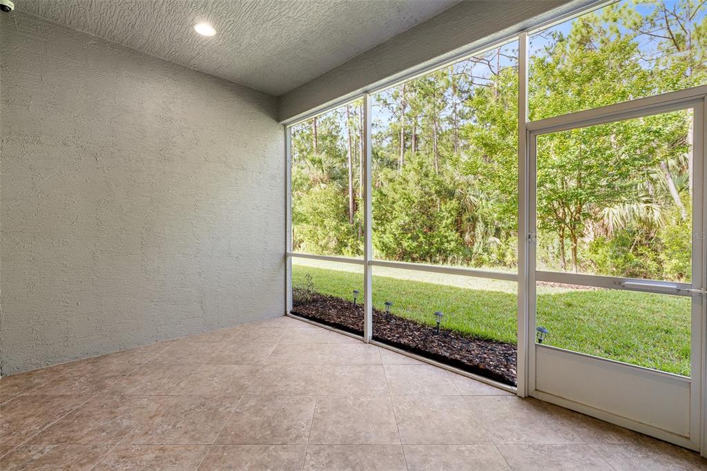 A screened-in patio with tile flooring, a textured gray wall, and a view of trees — 829 PINEWOOD DRIVE, ORMOND BEACH, FL
